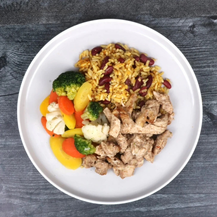 Top-down view of jerk chicken with coconut rice and beans and vegetables