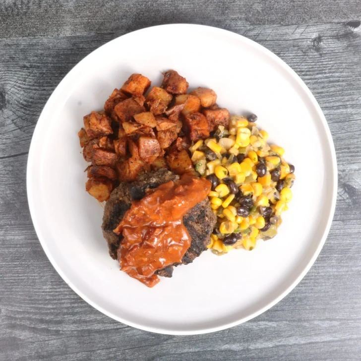 Top-down view of BBQ bacon and onion jam burger with potatoes and corn salad