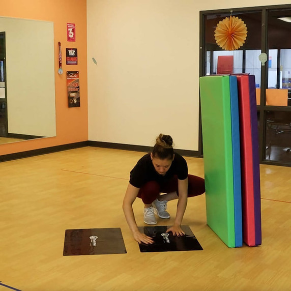 Coach places a pair of black Tumbl Trak Non-Slip Smart Mat Sheets under mats in a gym