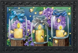 Briarwood Lane Fireflies Spring Doormat with lit candles and purple flowers on wooden stumps.