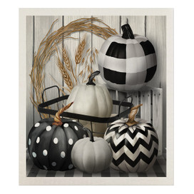 Black and white pumpkins with various patterns on a tray with dried wheat stalks nearby.