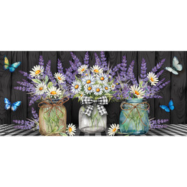Lavender and daisies in three glass jars with ribbons on a black and white surface.