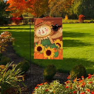 Briarwood Lane Happy Scarecrow fall garden flag displayed on a lawn with vibrant autumn flowers.