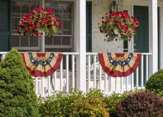 Briarwood Lane large patriotic bunting flags with applique hang on a porch with red flowers.