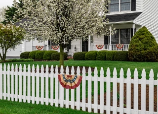Briarwood Lane large patriotic bunting flags with applique hanging on a white picket fence outdoors.