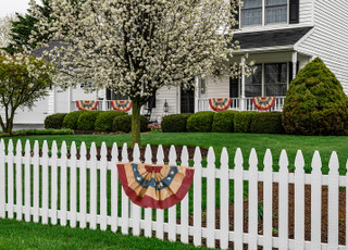 Briarwood Lane patriotic bunting on a white picket fence, aged USA american flag tea-dyed bunting.
