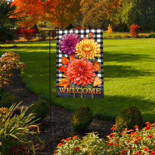 Checkered garden flag with vibrant orange, yellow, and purple mums and welcome text on stand outdoors.