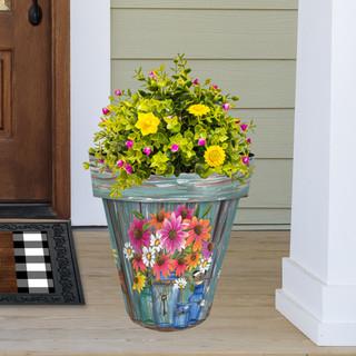 Large teal planter with colorful flower design holding green plants with yellow and pink flowers.