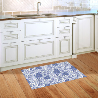 Blue and white floral doormat on wooden floor beside kitchen sink and white cabinets.