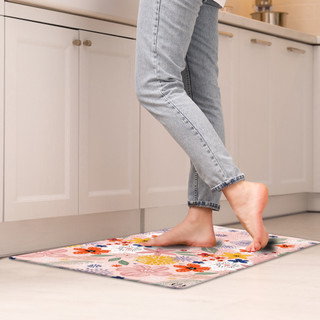 Bare feet on Colorful Flowers Comfort Mat in kitchen with white cabinets and light flooring.