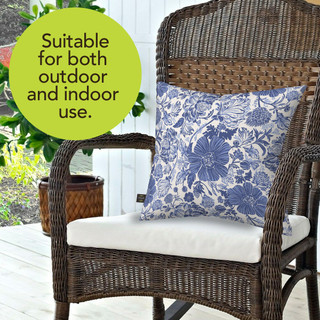 Blue and white floral burlap pillow on a wicker chair with white cushion.