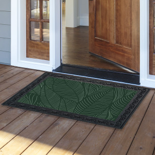 Green Tropical Leaves Doormat with black border on wooden porch outside open doorway entrance.