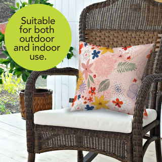 Colorful Flowers Burlap Pillow on a wicker chair with white cushion, pink background and multicolor flowers.