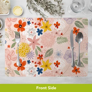 Pink floral placemat with colorful flowers, silverware, on white table with green leaves and herbs.