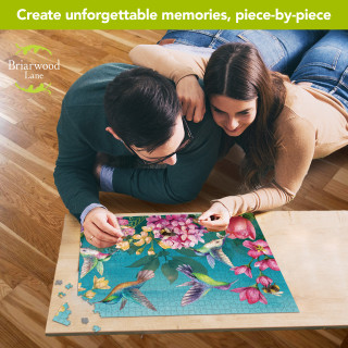 Couple working on Briarwood Lane Springtime Hummingbirds 1000-piece jigsaw puzzle on wooden floor together.