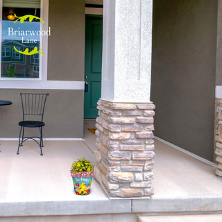 Bee Happy Beehive Small Planter with colorful flowers on a front porch next to a pillar.