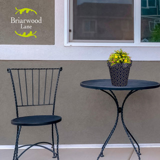 Small blue geometric planter with yellow flowers on a black metal table beside a chair outdoors.