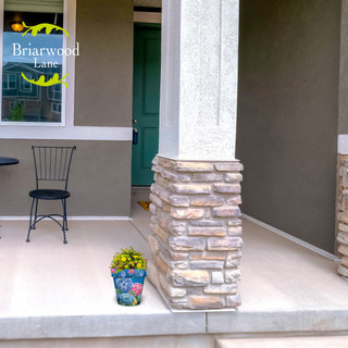 Small colorful hydrangeas in pot on beige porch with stone pillar and green door background.