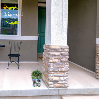 Small checkered snowman planter with green plant on a front porch next to a pillar.