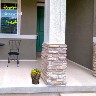 Small colorful floral planter with orange and teal hues on a house porch next to pillar.