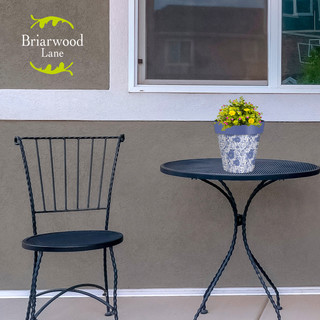 Small blue and white floral planter on a black metal table beside a matching chair outdoors.