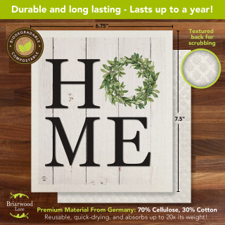 White Home Swedish Dishcloth with green wreath on a wooden background, 6.75 x 7.5 inches.