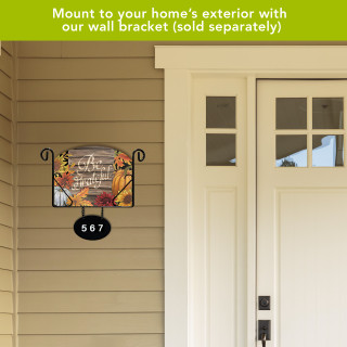 Be Grateful colorful acrylic art sign with black metal bracket and house number on beige siding.