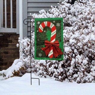Festive Candy Cane Burlap Garden Flag with red bow and snowflakes on green background displayed outdoors.