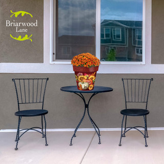 Fall Beauty Medium Planter with orange flowers on a small black table between two chairs.
