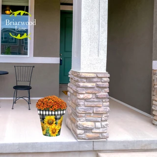 Medium Checkered Sunflowers Decorative Planter with orange flowers on a porch beside a pillar outdoors.