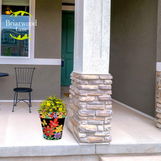 Whimsy Flowers Medium Planter with colorful floral design and vibrant yellow flowers on a porch.