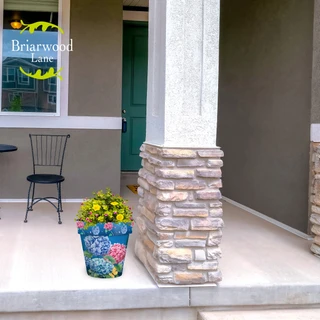 Vibrant hydrangeas in colorful medium planter on a porch with a stone pillar and chair.