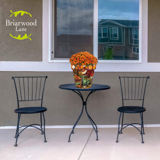 Autumn Farm Medium Planter with orange flowers on small black outdoor table between two black chairs.