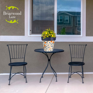 Citrus and Vines medium planter on outdoor table between two black metal chairs with yellow flowers.