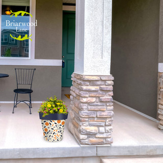 Citrus and Vines medium planter with yellow flowers on a porch next to a stone pillar.