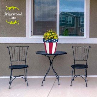 American Flag Medium Planter with yellow flowers on a small table between two black metal chairs.