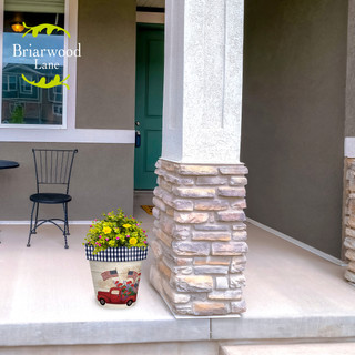 Stars and Stripes Truck Medium Planter with yellow flowers on a front porch next to pillar.