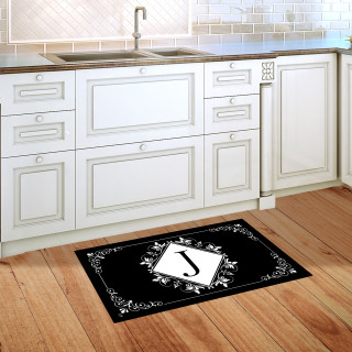 Black and white monogram doormat with floral design and letter J on wooden kitchen floor.