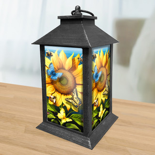 Black metal Sunflower Dance Lantern with vibrant yellow sunflowers and blue butterflies on a wooden table.
