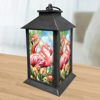 Black metal Flamingo Pair Lantern with pink flamingos and floral design on a wooden table indoors.