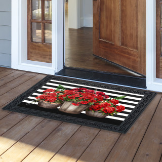Black doormat with white stripes and red geraniums on a wooden porch outside an open doorway.