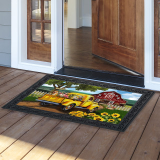 Flower Farm Doormat with colorful truck, sunflowers and barn design on wooden porch outside doorway.