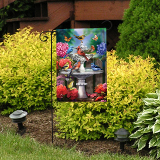 Spring Bath Birds Garden Flag with colorful birds, butterflies, and flowers on a garden stand outdoors.