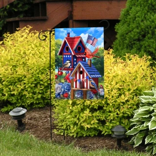 Garden flag with patriotic birdhouses and American flag design on a decorative stand outdoors.