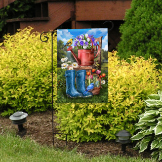 Garden flag with blue boots, red watering can, and colorful flowers on display outdoors.