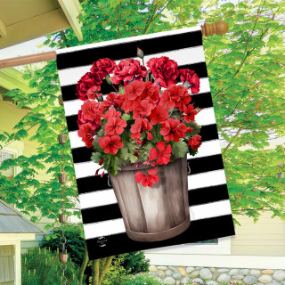 Red geraniums in a metal bucket on a black and white striped house flag outdoors.