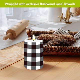 Black and white check flameless candle on wooden table with lit flame.