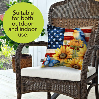 American Country Indoor/Outdoor Pillow with sunflower, blue bird, and American flag design on wicker chair.