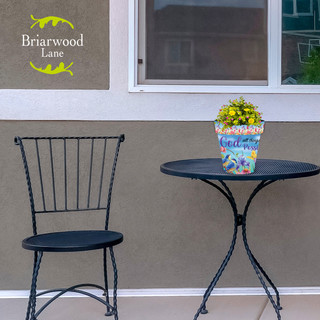 Briarwood Lane With God Small Planter with yellow flowers on a black metal table and chair.