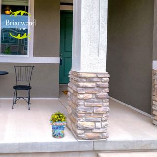 Small blue floral planter with yellow flowers on a house porch next to stone pillar base.